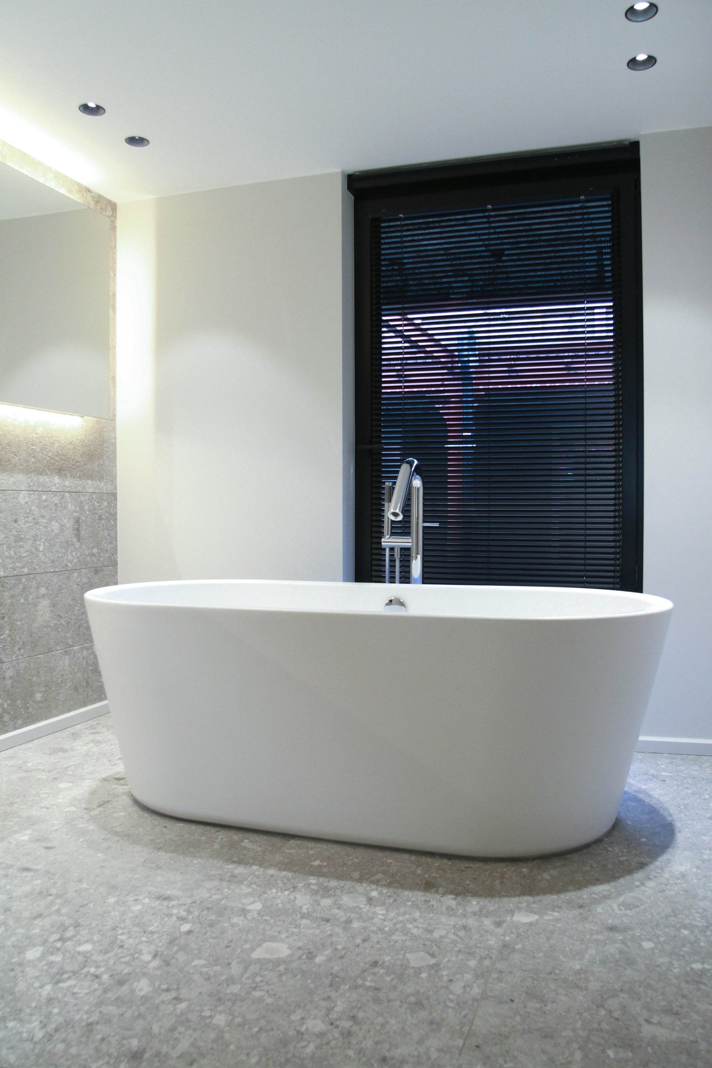 Salle de bain rénovée, baignoire îlot blanche sur un sol en pierre gris clair