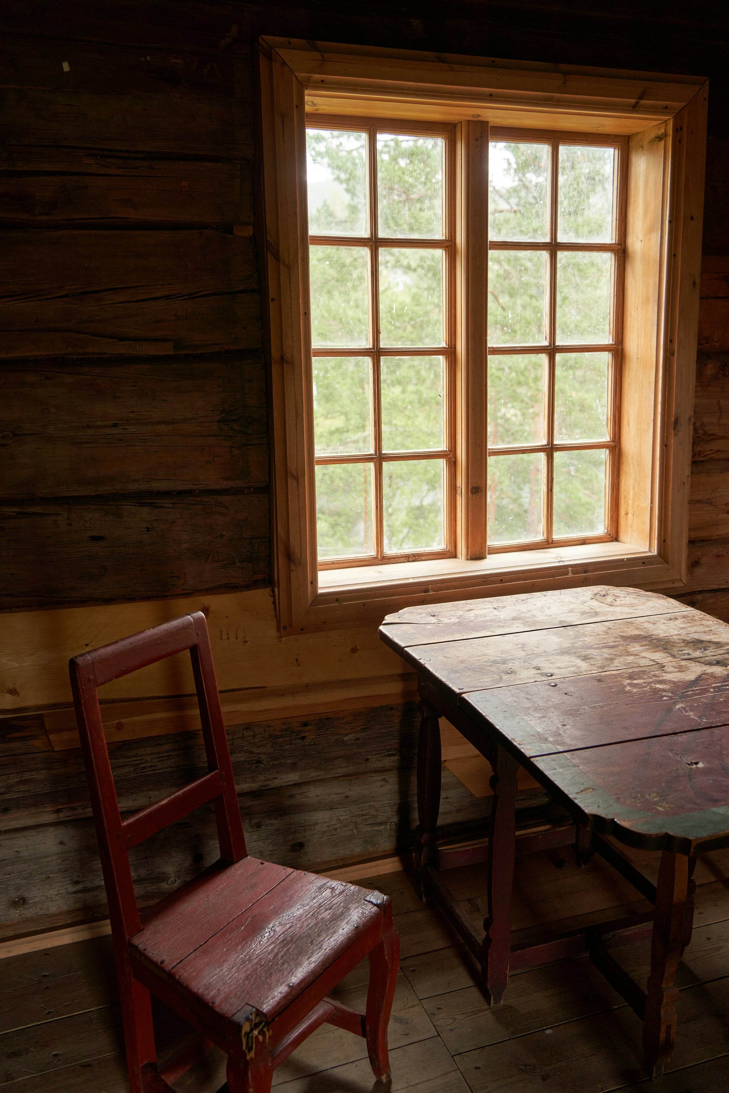 Pièce aux madriers sombres, petite fenêtre à petits bois, chaise peinte et table ancienne