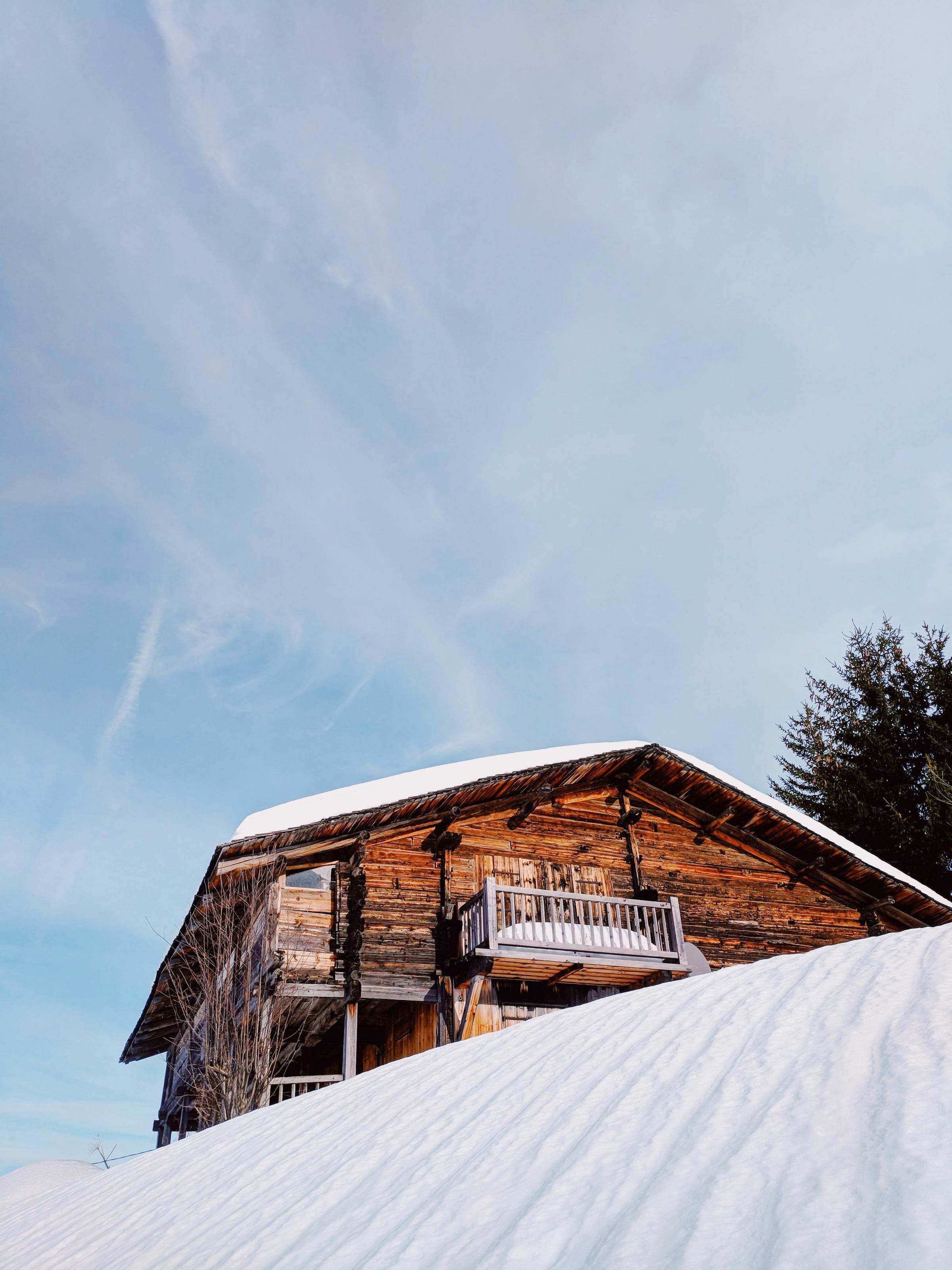 Chalet en madriers brunis et balcon en bois sur une pente enneigée, ciel d’hiver clair
