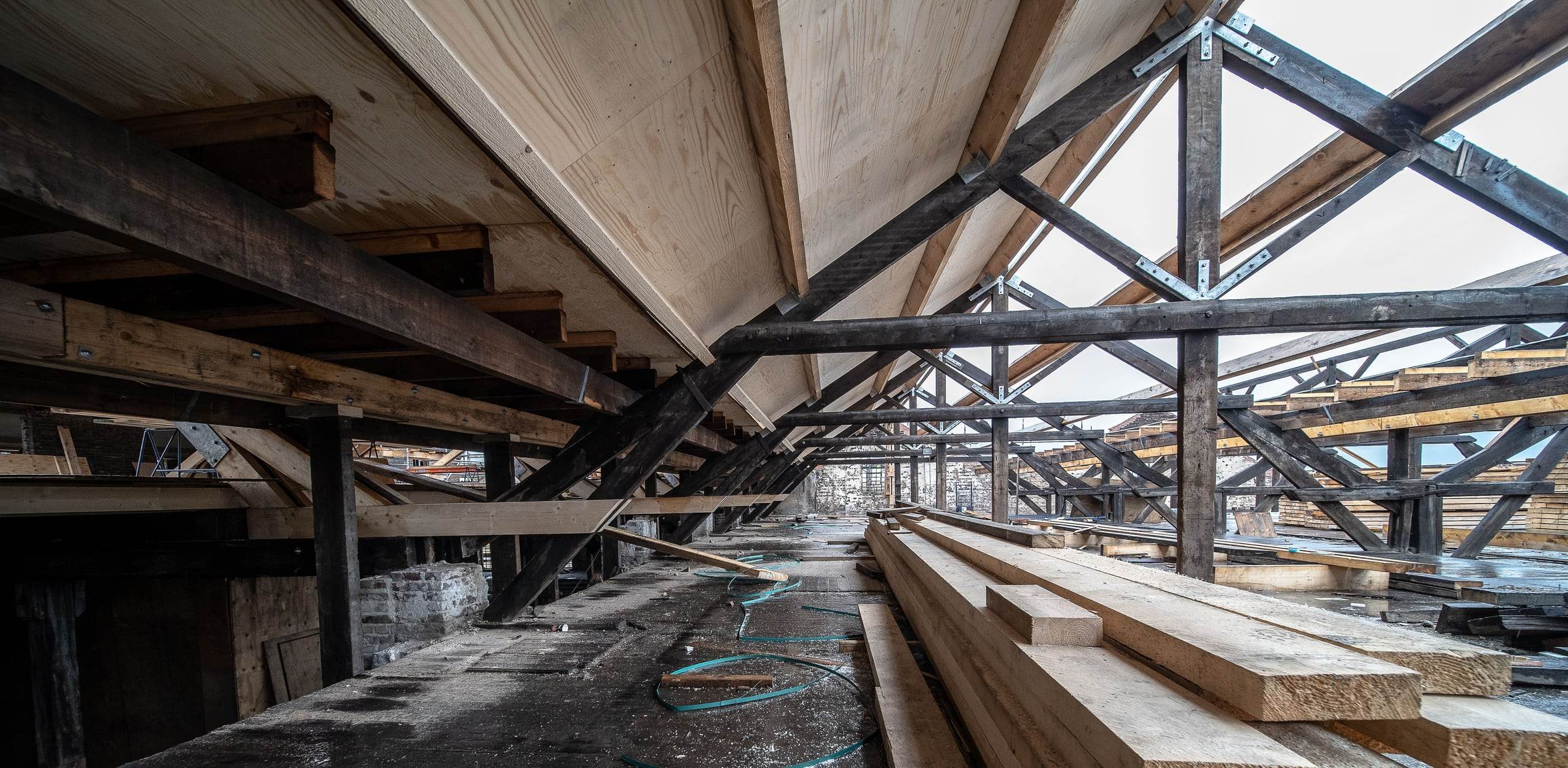 Charpente ancienne aux bois sombres et panneaux de toiture neufs en bois clair pendant les travaux
