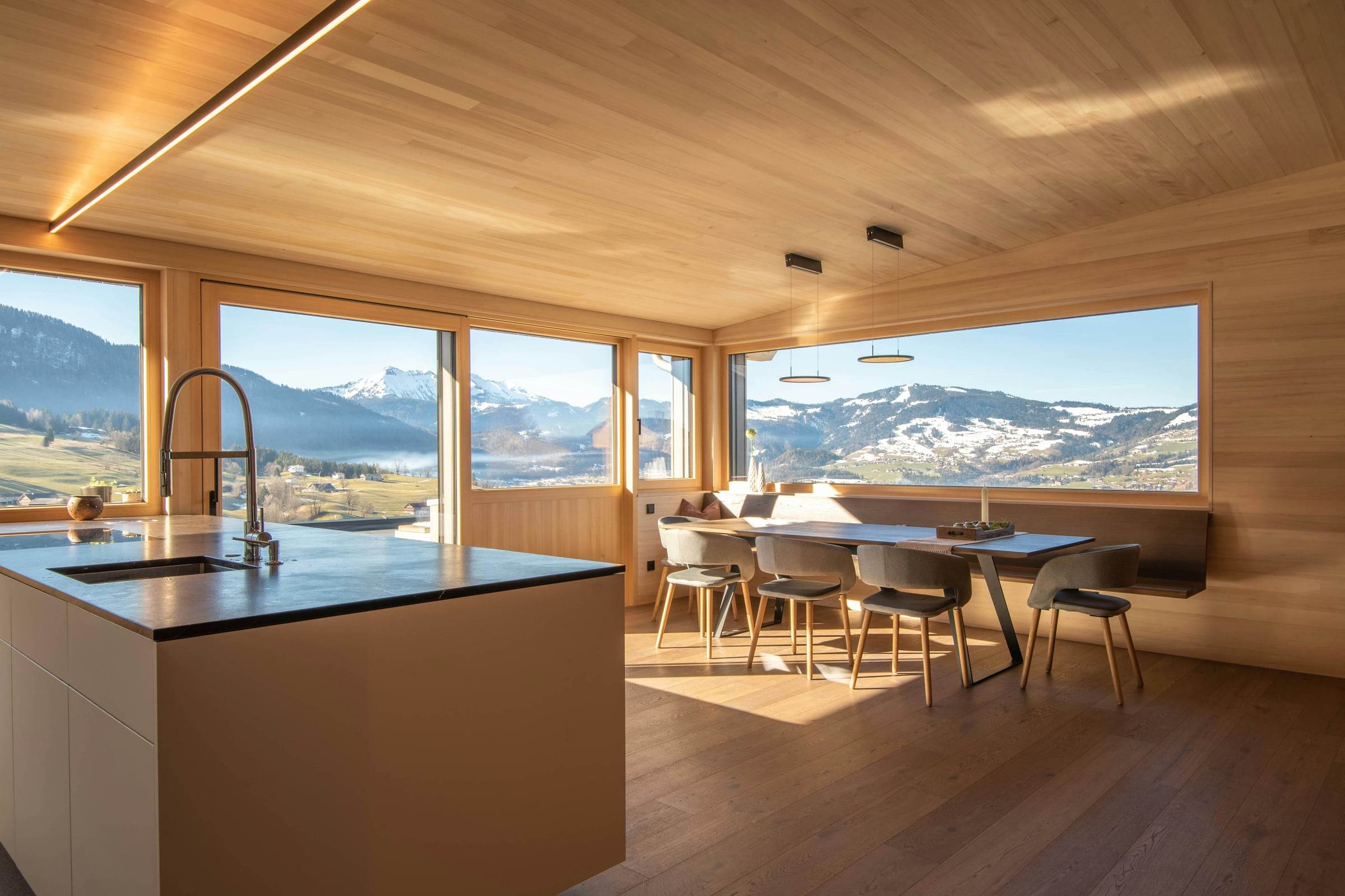 Séjour et cuisine en bois clair, grandes baies sur la montagne enneigée