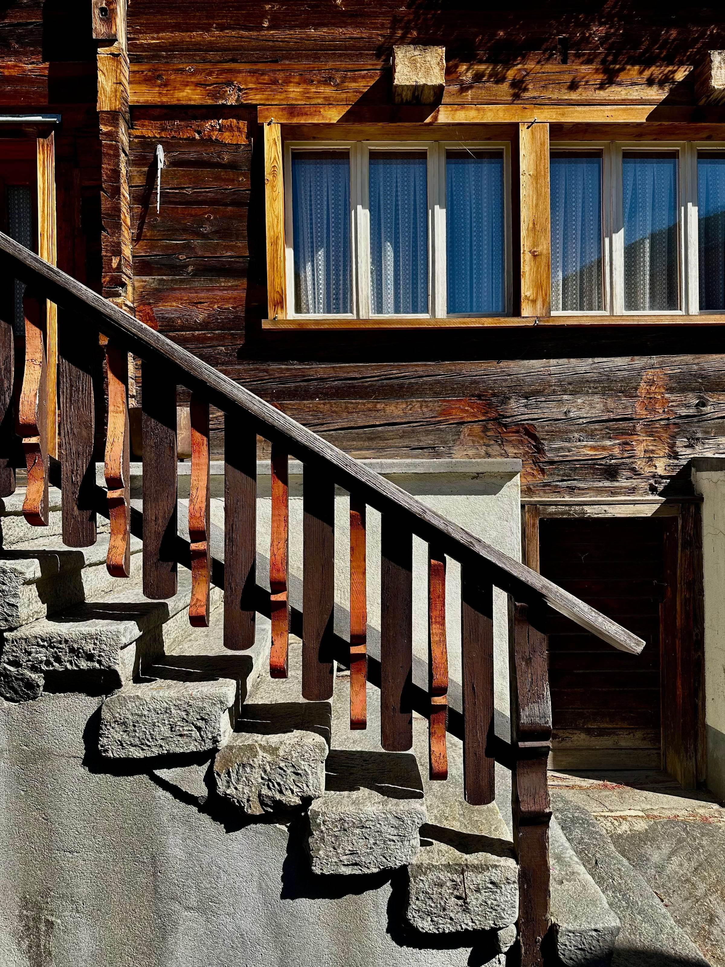 Escalier extérieur en dalles de pierre et garde-corps en bois devant une façade en madriers brunis