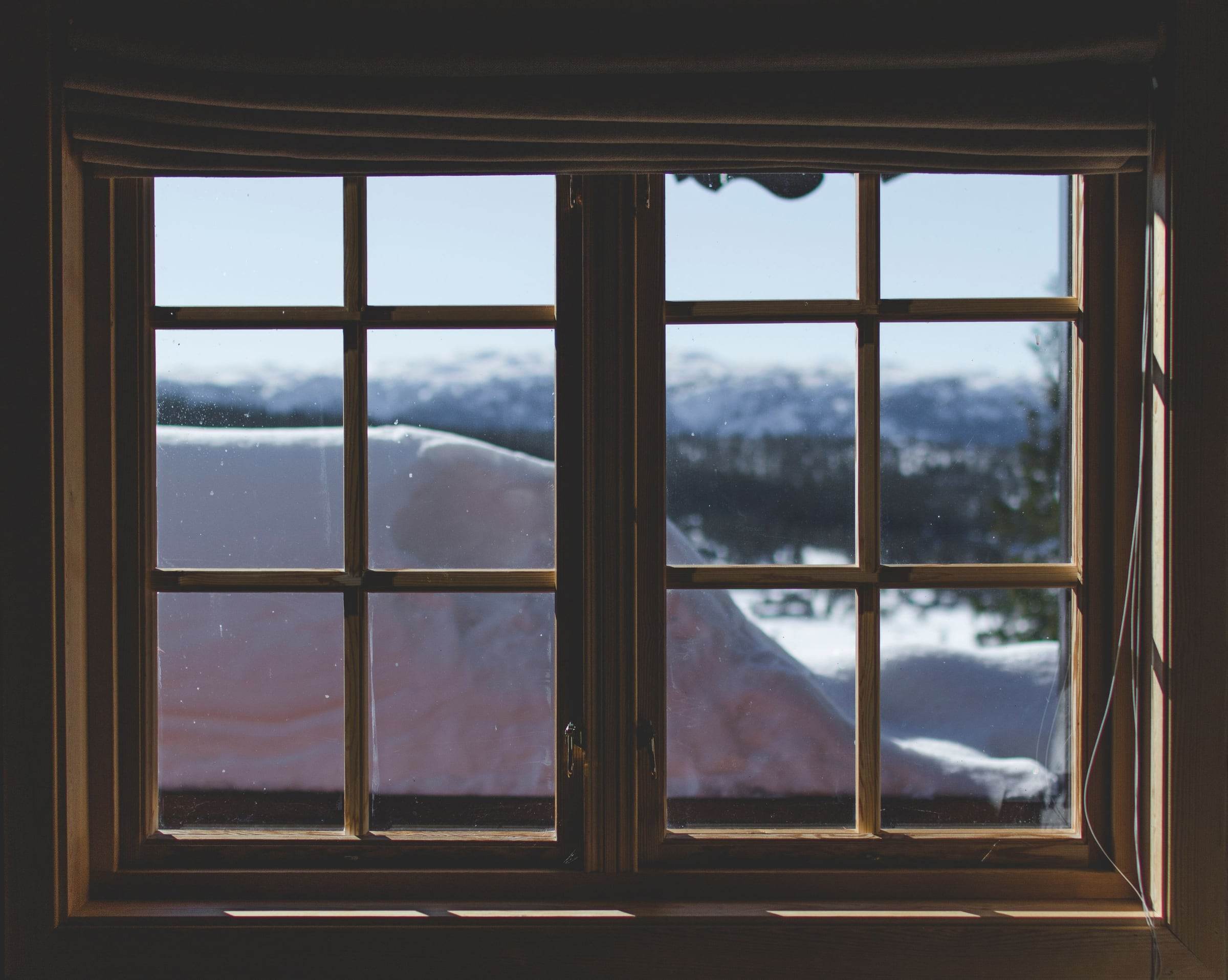 Double fenêtre en bois à petits bois vue de l’intérieur, neige et forêt derrière les carreaux